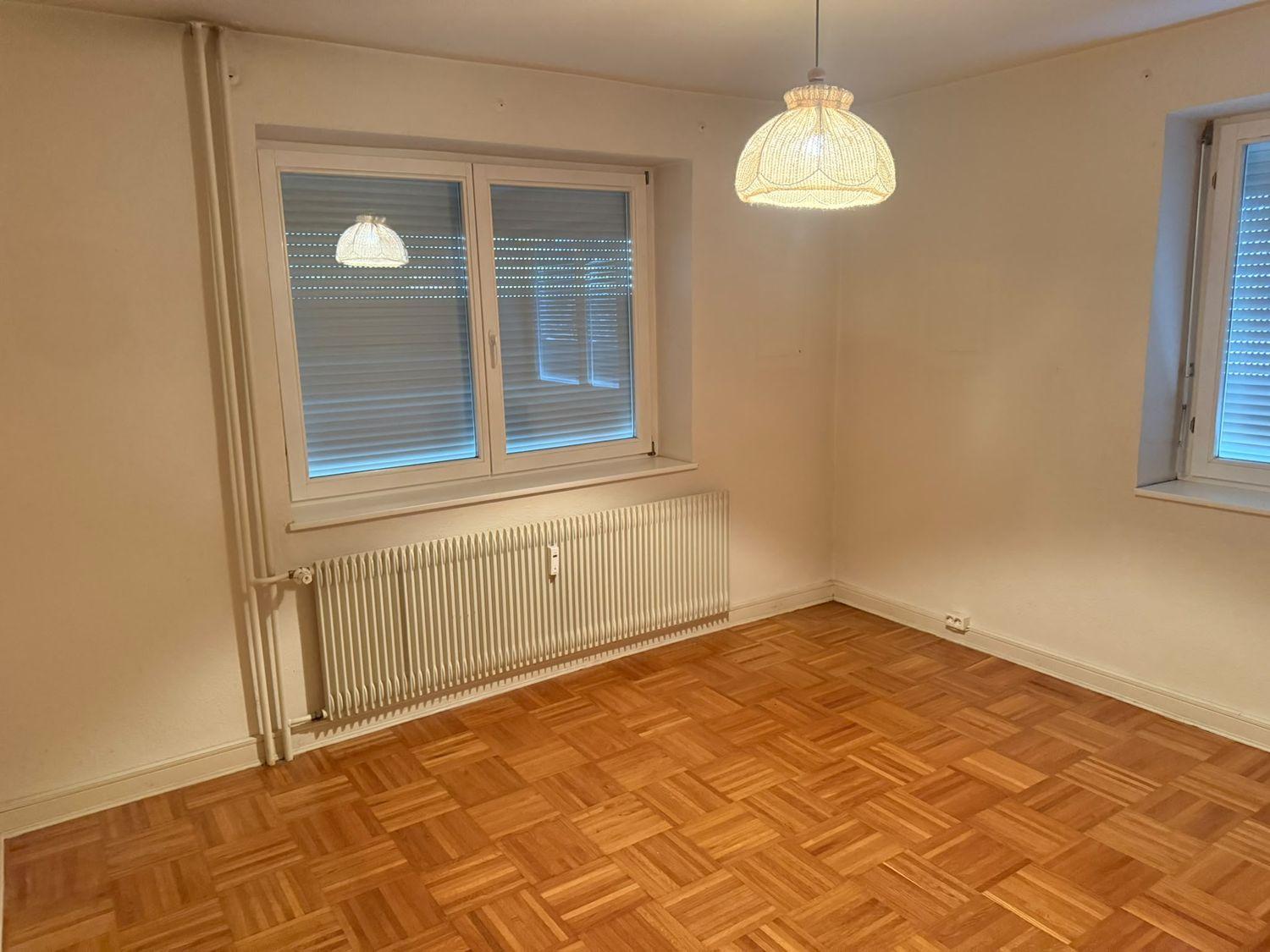 Leer geräumtes Zimmer mit Parkettboden und zwei Fenstern